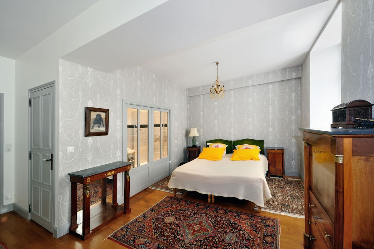A bedroom with a bed, a nightstand, a dresser, a window, and a door.