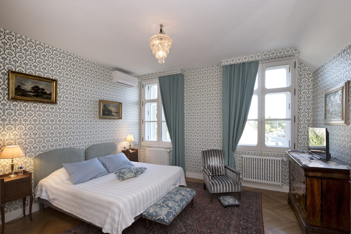 A bedroom with a bed, a chair, a desk, and a chandelier.
