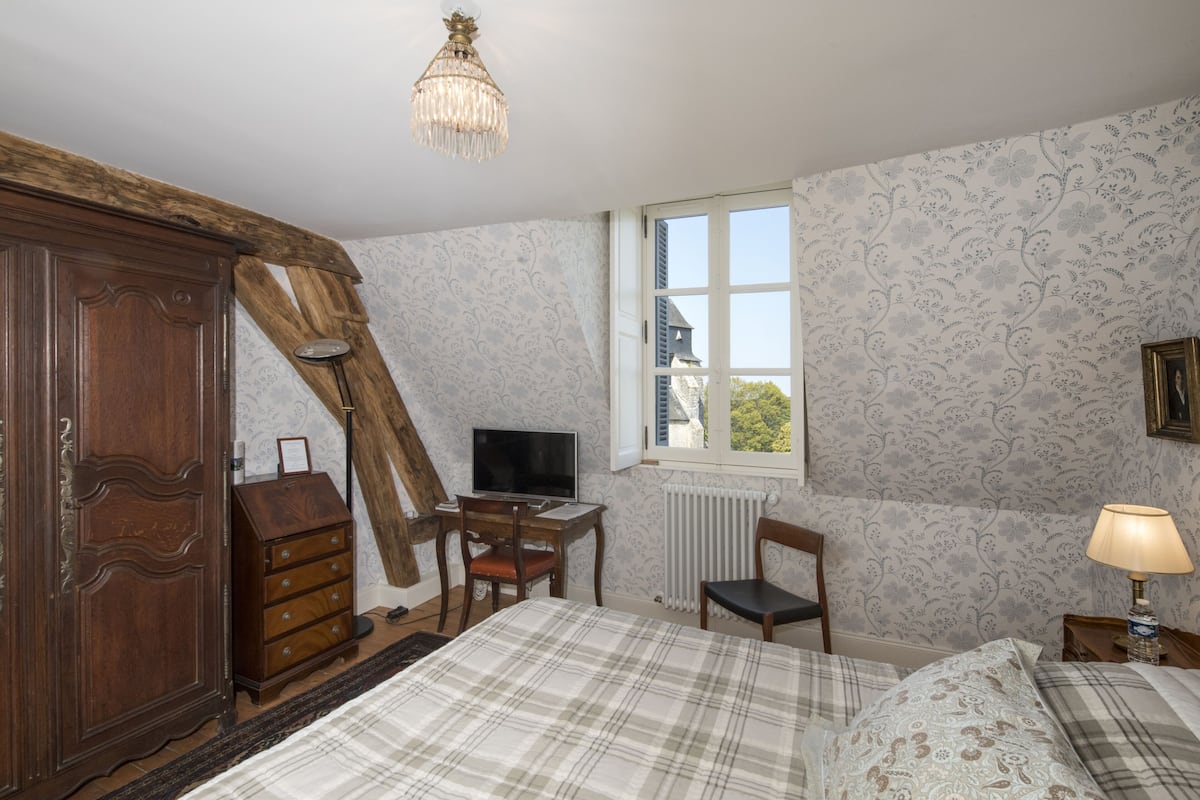 A bedroom with a bed, wooden wardrobe, desk, chair, television, and a window with a view.