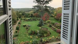 A view of a well-maintained garden with various plants and trees, viewed through open window shutters. - Le Prieure d'Orchaise (Valencisse)