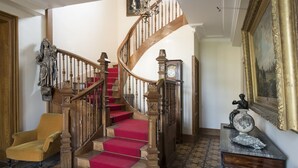 A grand staircase with red carpeted steps, a wooden railing, and a clock on the wall. - Le Prieure d'Orchaise (Valencisse)