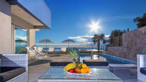 A poolside area with lounge chairs, a table with fruit, and a view of the ocean.