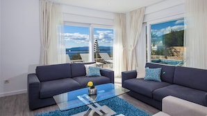 A modern living room with two dark sofas, a glass coffee table, and a view of the sea through large windows.