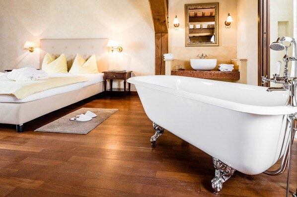 A bedroom with a large white bathtub, a wooden floor, a bed with white bedding, and a small bedside table with a lamp. - Poggio Antico - Suites and Breakfast (Monte San Vito)