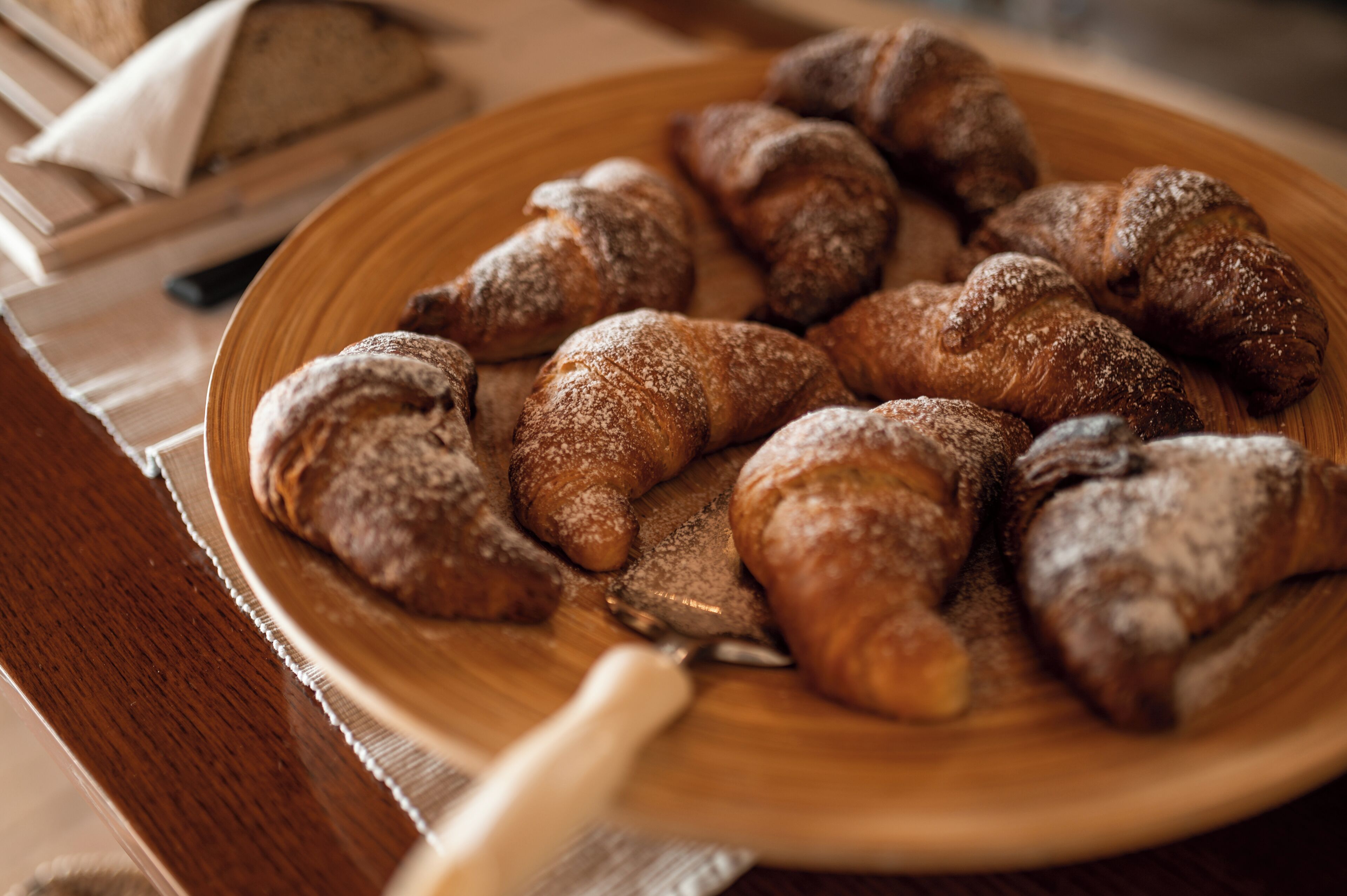 Une assiette en bois contenant plusieurs pâtisseries, notamment des croissants et une baguette, posée sur une table.