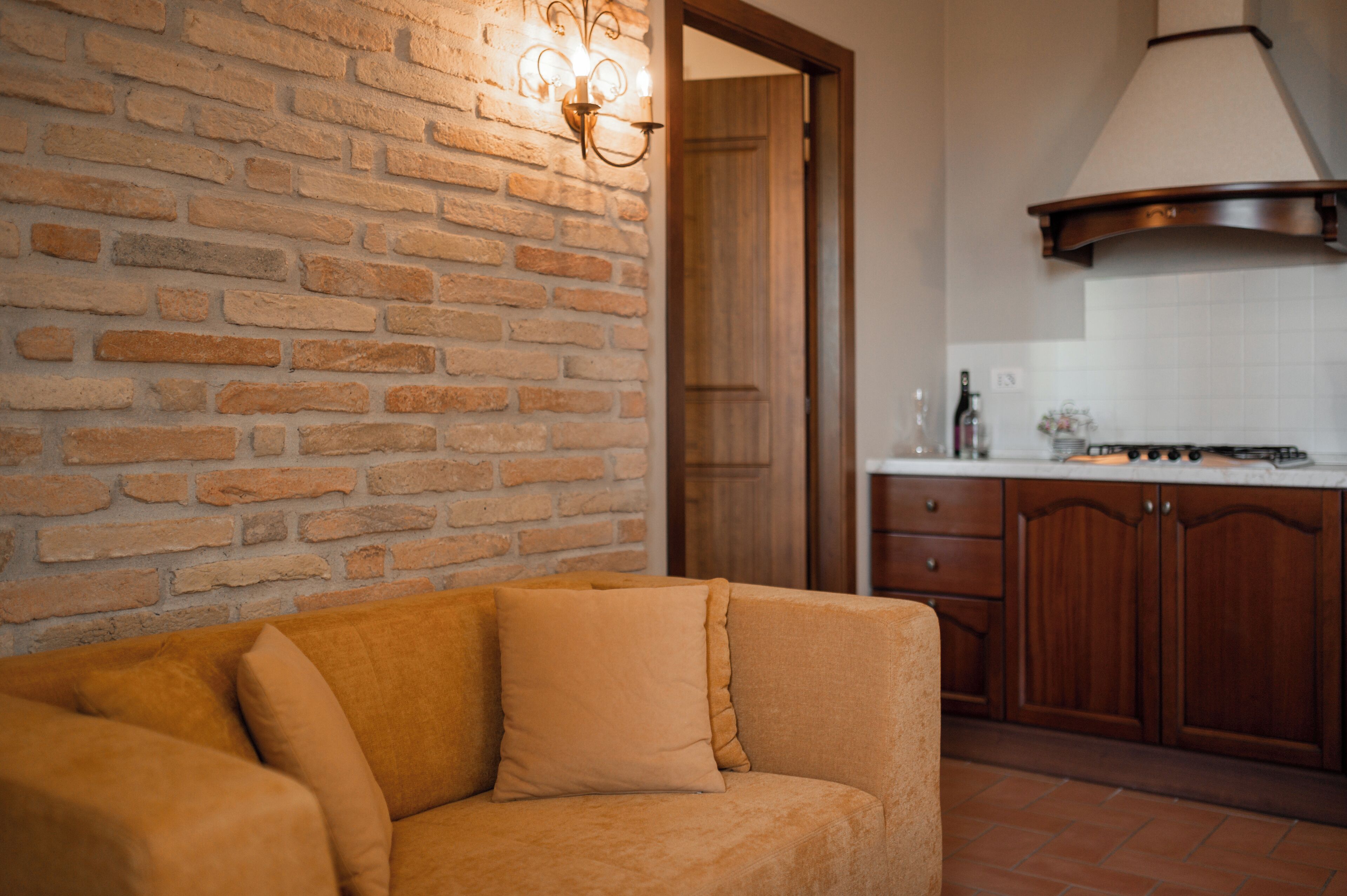 A living room with a brick wall, a sofa, and a kitchen area with wooden cabinets and a stove.