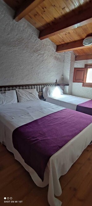 A room with two beds, wooden beams on the ceiling, and a window with wooden shutters.