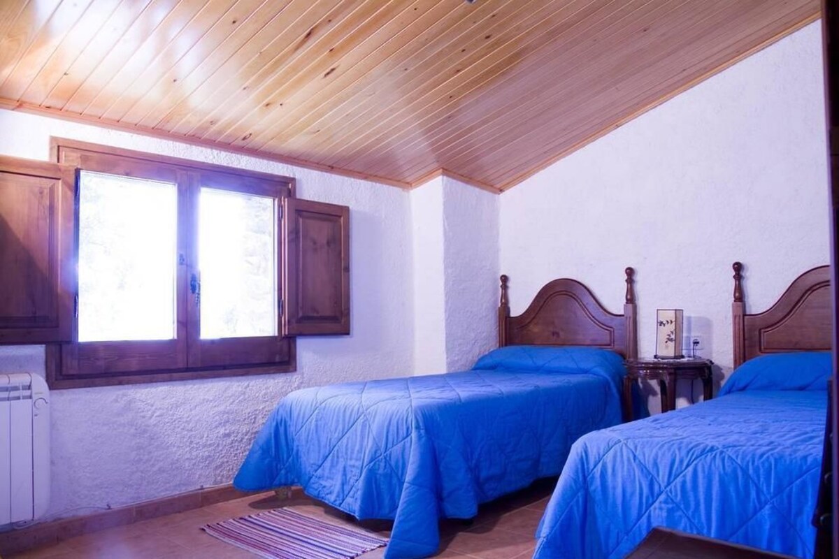 A bedroom with two wooden beds, a window with shutters, and a radiator.