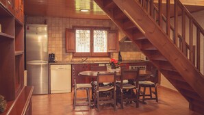 Una cocina con armarios de madera, un refrigerador de acero inoxidable, un lavavajillas, un ventanal con cortinas de encaje y una escalera de madera.