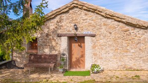 Un edificio de piedra con una puerta de madera, un banco, un pequeño jardín y un letrero que dice "CAUBET 3".