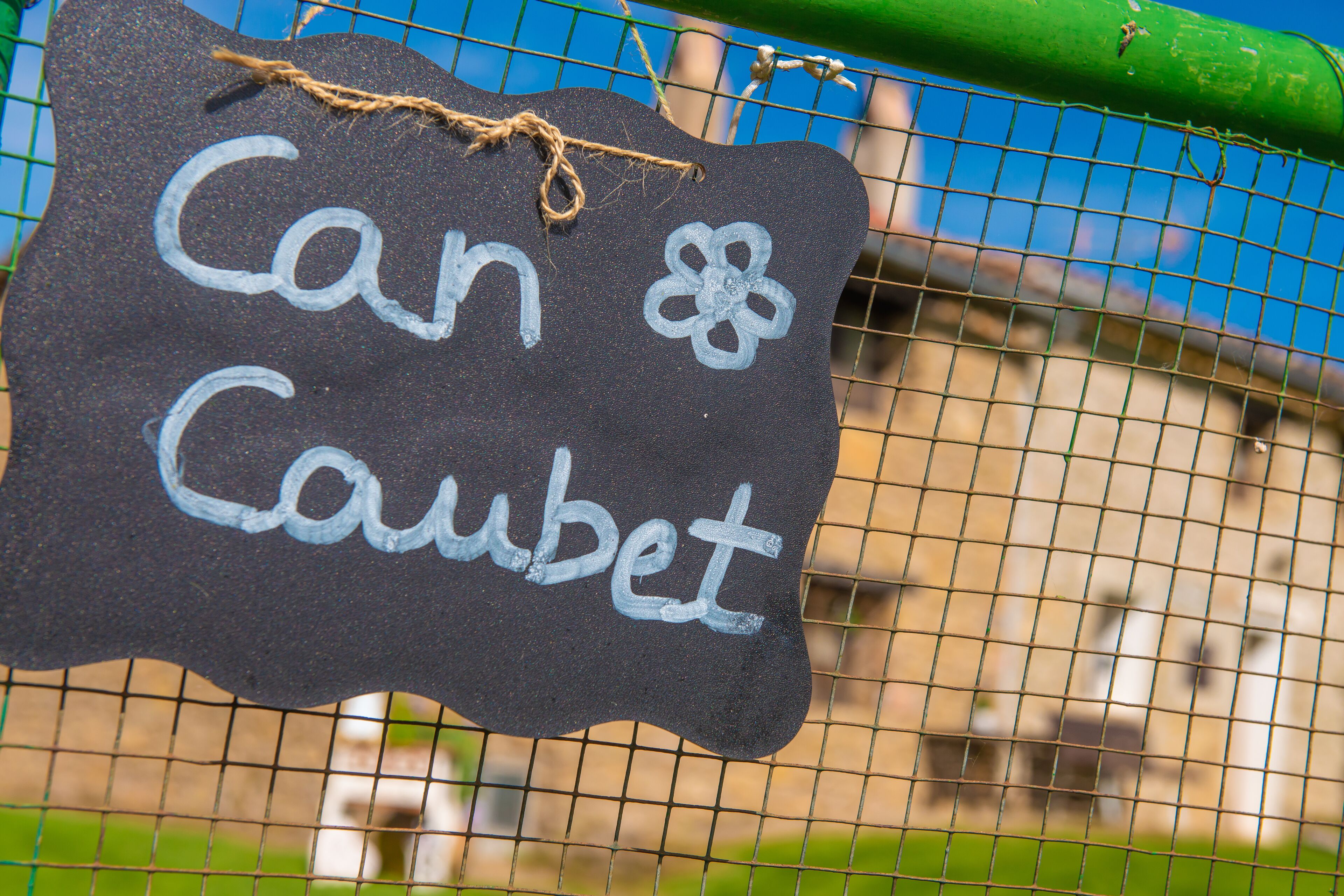 Un letrero de pizarra con el texto 'Can & Coubet' colgado de una cerca.