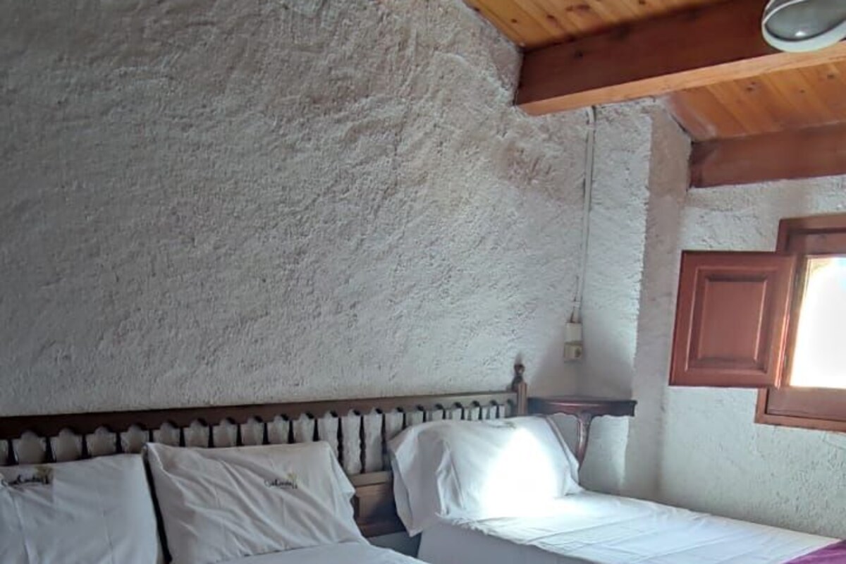 A room with two beds, wooden beams on the ceiling, and a window with wooden shutters.