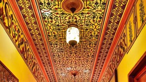Um corredor com detalhes ornamentais no teto, um banco com almofadas e quadros nas paredes.