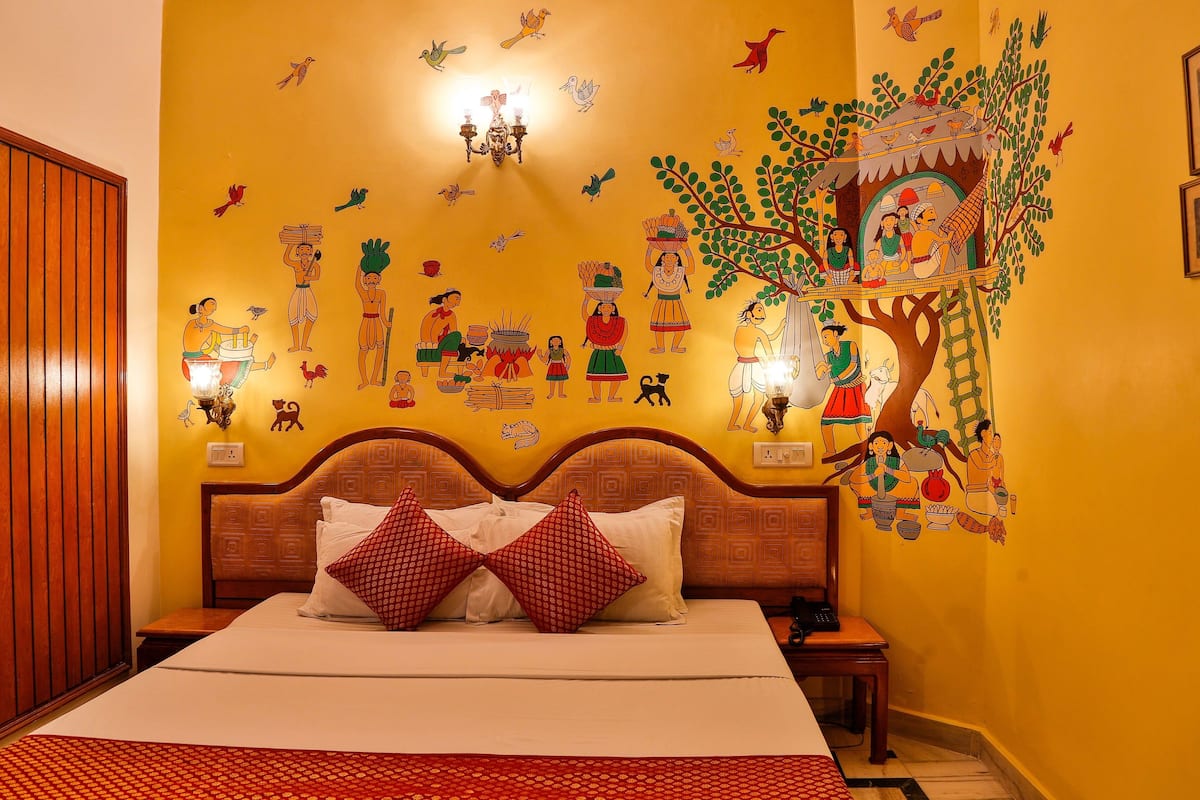 A hotel room with a large bed, wooden headboard, and a mural depicting cultural scenes on the wall.