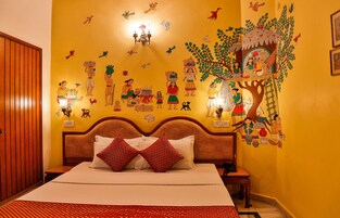 Quarto de hotel com uma cama grande, cabeceira de madeira e um mural retratando cenas culturais na parede.