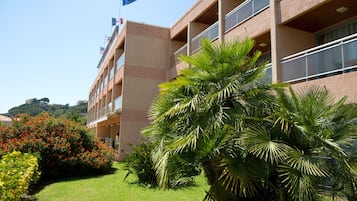 Un immeuble à plusieurs étages doté de balcons, entouré d’une végétation luxuriante et de plantes en fleurs.