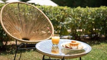 A wicker chair and a small round table with a glass of orange juice and pastries on a grassy lawn.
