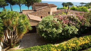 A coastal villa with stone walls, a garden with various plants, and a view of the sea. - Hôtel La Pinède (Ajaccio)