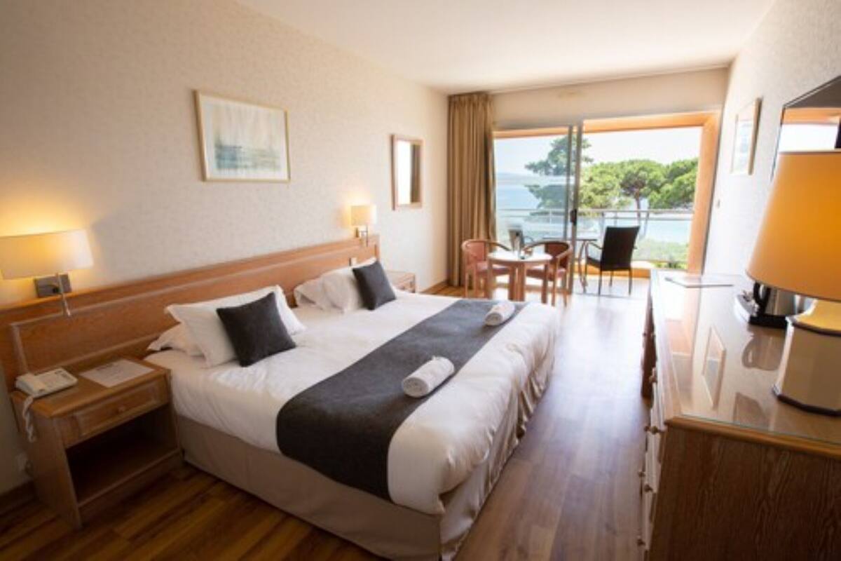 A hotel room with a large bed, a desk, a chair, and a view of the sea.