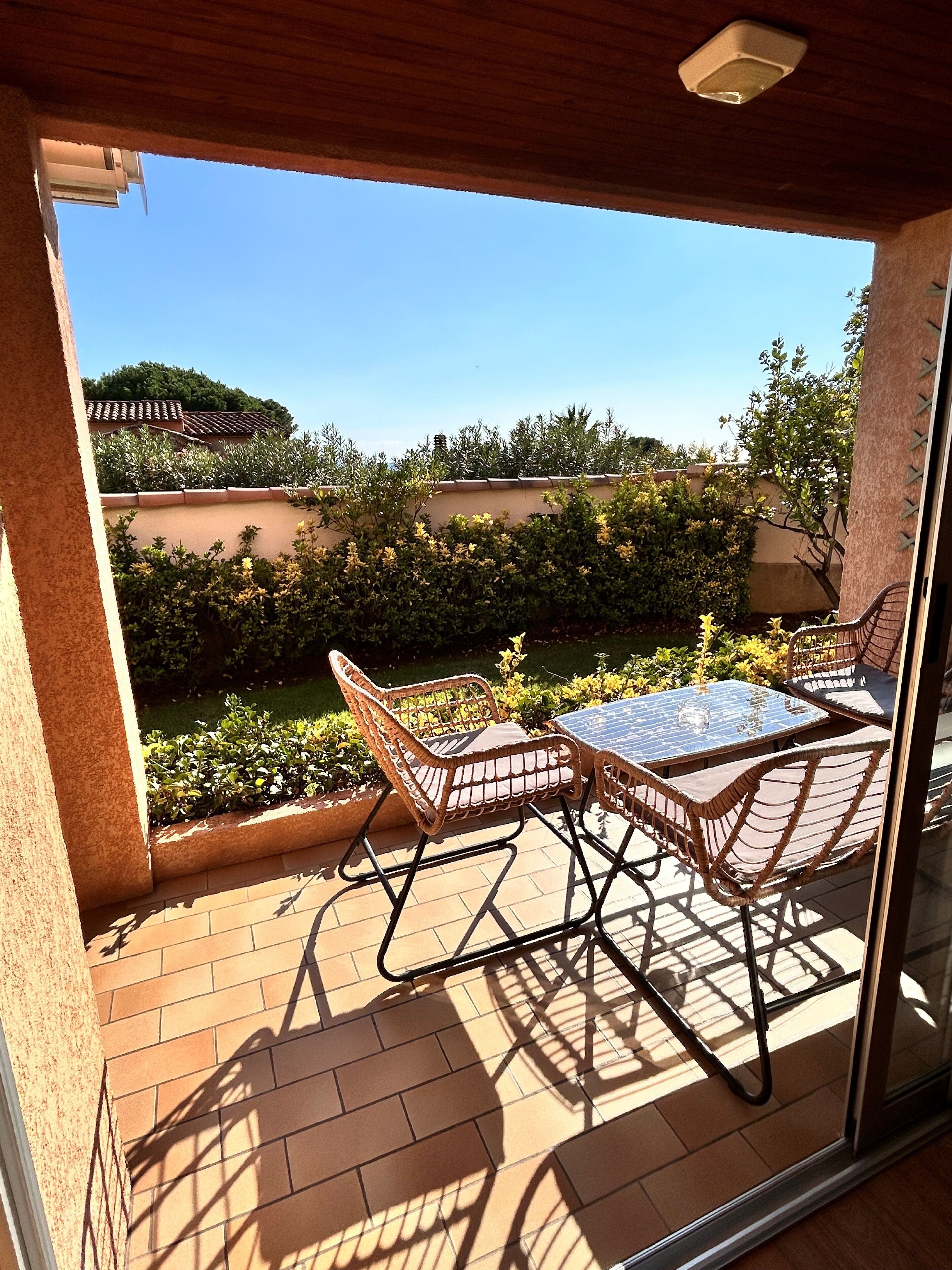 A patio with wicker furniture and a glass table, overlooking a garden with a tiled roof and greenery.