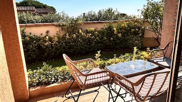 A patio with wicker furniture and a glass table, overlooking a garden with a tiled roof and greenery.