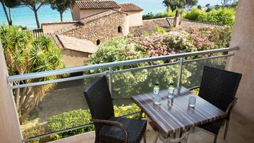 A balcony with a table and chairs, overlooking a coastal area with buildings and greenery.