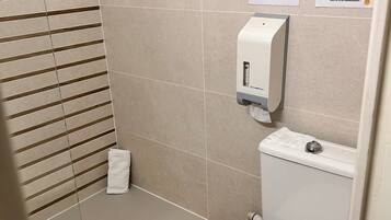 Un baño con inodoro, secamanos y dispensador de toallas de papel. Hay señales de advertencia en la pared.