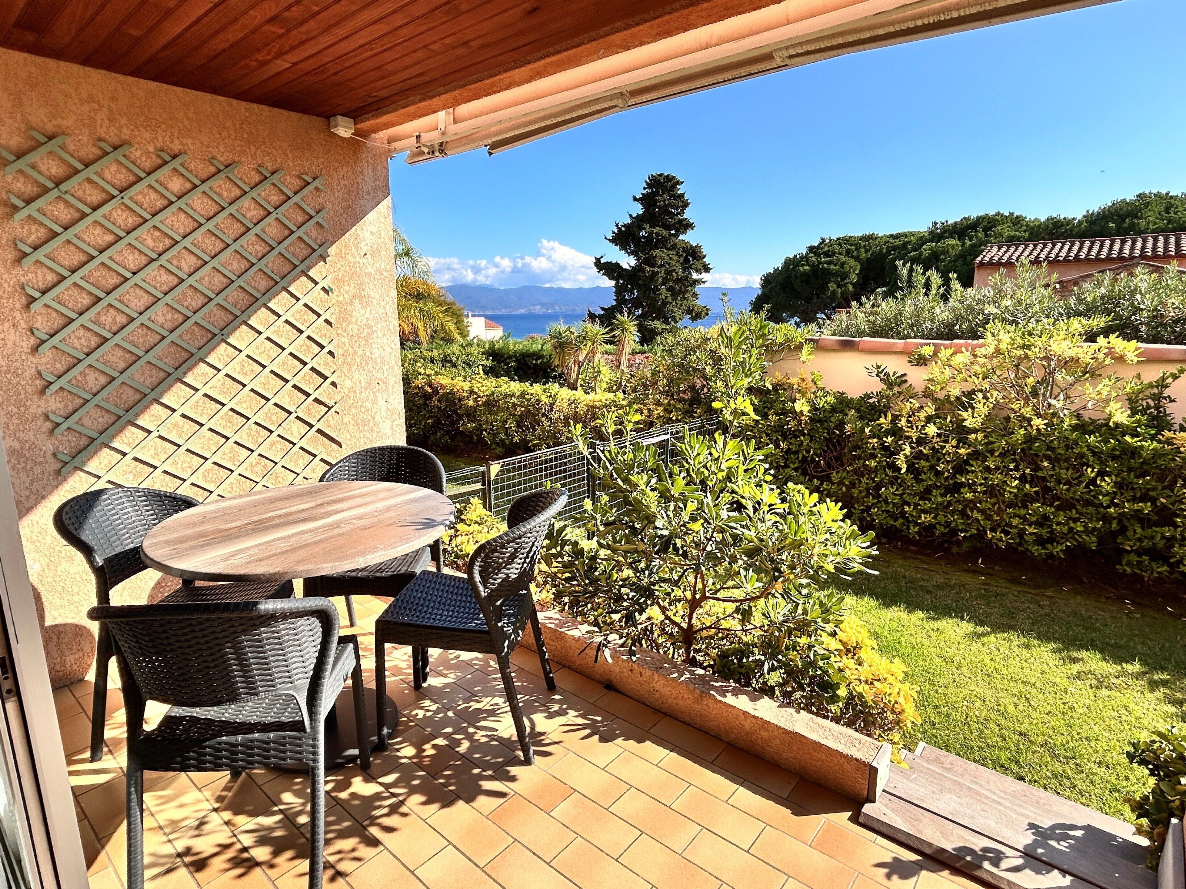 A patio with a table and chairs, a pergola, and a view of a garden and mountains.