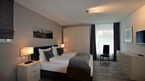 A modern hotel room with a large bed, bedside tables, a wardrobe, a desk, and a chair.