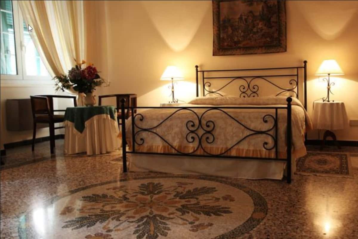 A bedroom with a bed, two bedside lamps, a chair, a table, and a vase of flowers.