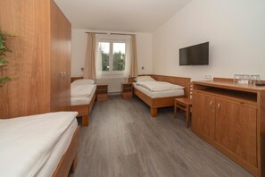 A hotel room with two single beds, a wooden wardrobe, a TV, and a window with curtains.