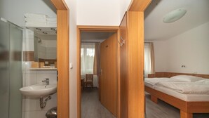 A hotel room with a wooden bed, a bathroom with a sink, and a shower. - Hotel Pansky dum (Blovice)