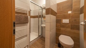 A modern bathroom with a glass-enclosed shower, a white toilet, and a wooden floor. - Hotel Pansky dum (Blovice)