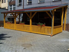 A yellow outdoor seating area with a metal roof, surrounded by brick walls and windows.