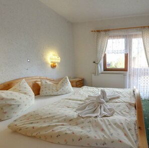 Un dormitorio con cama de madera, ropa de cama floral, una lámpara de pared y una ventana con cortinas.