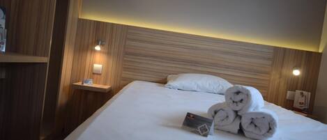Une chambre d’hôtel avec un lit bien fait, une table de chevet avec une lampe et une tête de lit en bois.