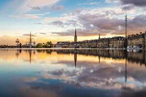 Paisagem urbana com uma torre imponente refletida em águas calmas, cercada por edifícios históricos.