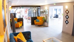 A modern lobby with a blue sofa, yellow and brown cushions, and a glass-top coffee table. - Best Hotel Bordeaux Sud (Villenave-d'Ornon)