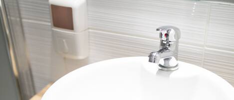 A bathroom with a white sink, wooden vanity, and a soap dispenser.