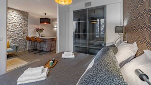 Ett modernt sovrum med en stor säng, en matplats med en vägg av sten och ett badrum med glasväggar.