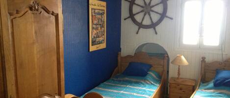 A bedroom with two wooden beds, a ship's wheel on the wall, and a door with intricate carvings.