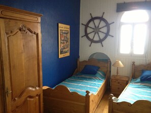 A bedroom with two wooden beds, a ship's wheel on the wall, and a door with intricate carvings.
