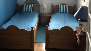 Ein Zimmer mit zwei Holzbett, ein Steuerrad, ein Fenster mit weißem Rahmen und eine Lampe auf einem Nachttisch.