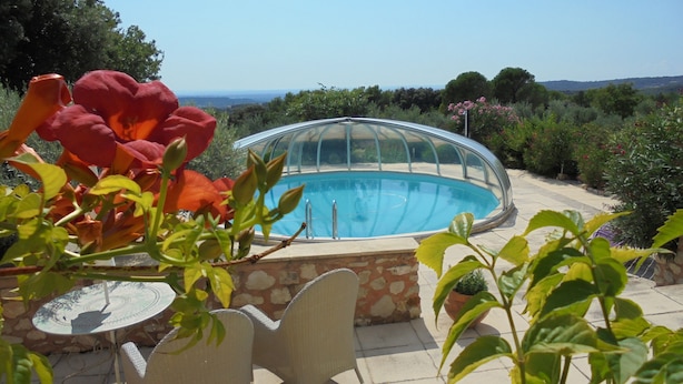 Una piscina con cerramiento de vidrio, rodeada de vegetación y un muro de piedra.