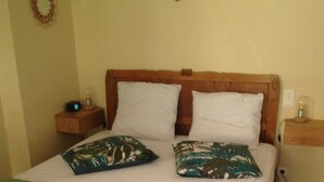Una cama con cabecera de madera, dos almohadas blancas, una colcha verde y una mesita de noche con una lámpara.