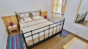 Een slaapkamer met een houten hoofdbord, een bed met gestreepte kussens, een nachtkastje met een lamp, een klein houten tafeltje en een spiegel aan de muur.
