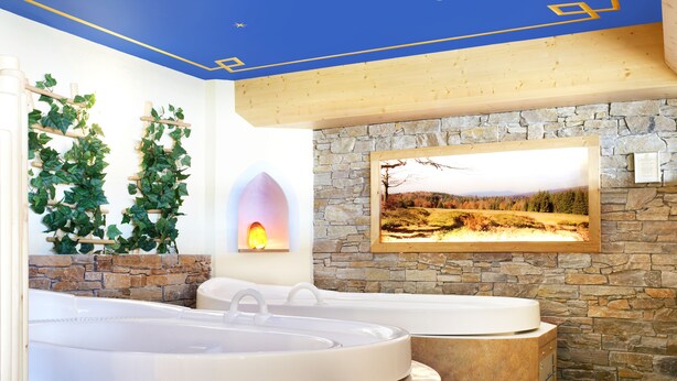 Un baño moderno con pared de piedra, un cuadro grande de un paisaje enmarco y una bañera independiente.