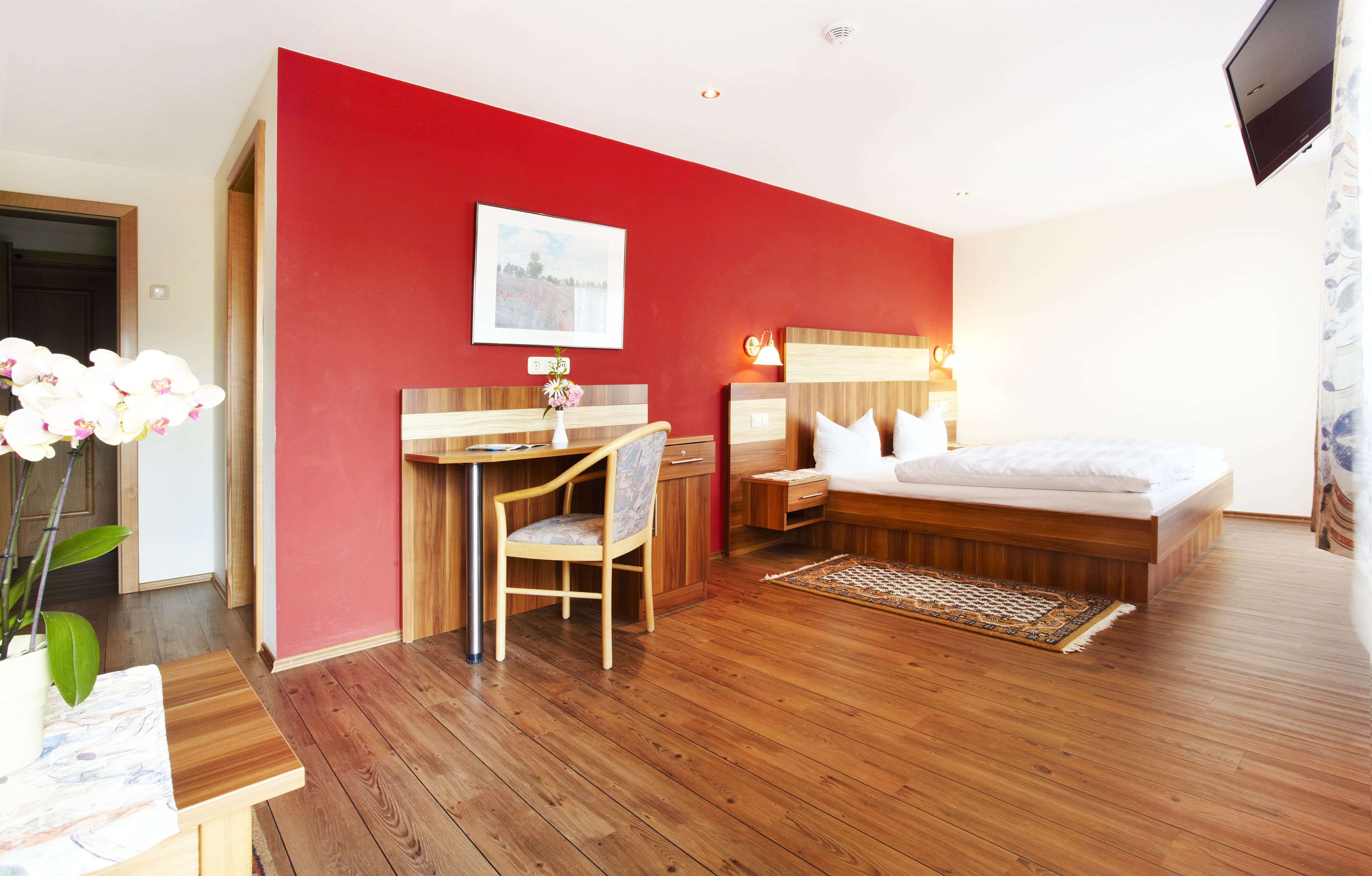 Une chambre d’hôtel avec un plancher en bois, un lit avec une literie blanche, un bureau avec une chaise, une table de chevet et un téléviseur fixé au mur.