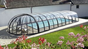 Una piscina con cerramiento de vidrio, rodeada de césped y flores.
