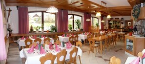 Un restaurant doté de nombreuses tables et chaises, de grandes fenêtres avec des rideaux et de luminaires suspendus.